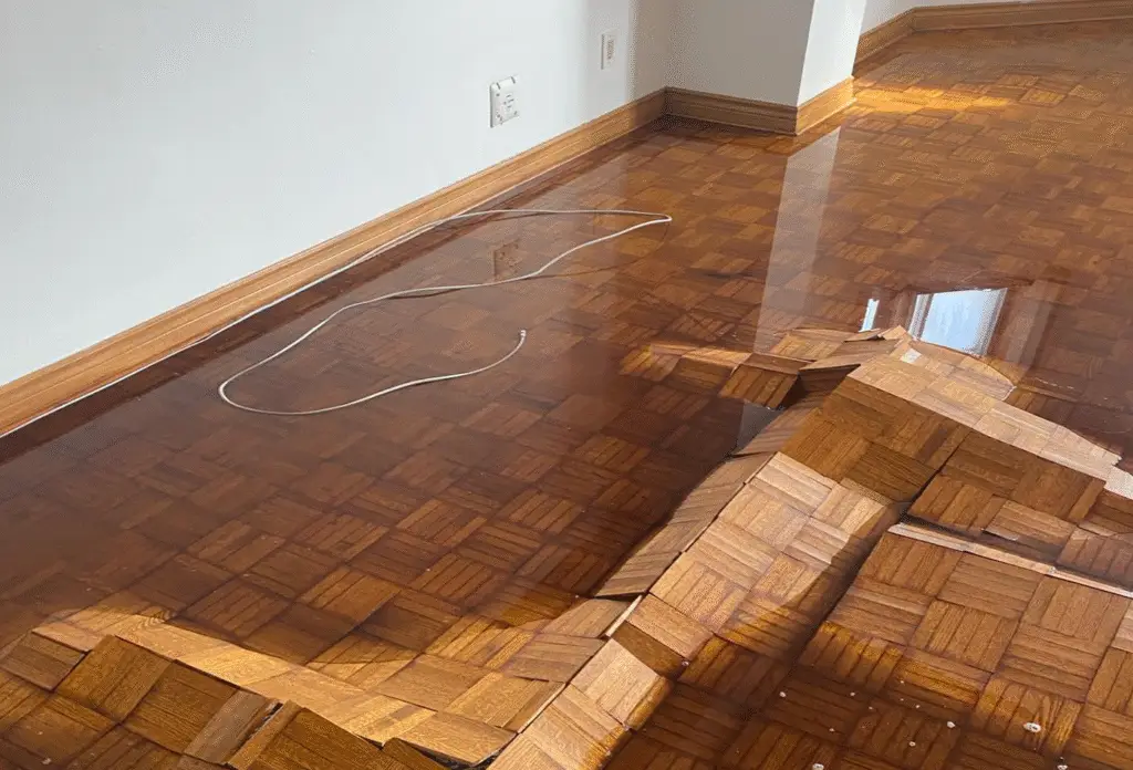 Buckled parquet hardwood floor lifted by flood water damage, awaiting property flood restoration