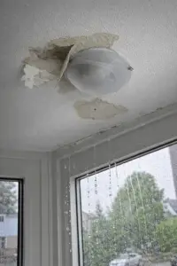Ceiling and window corner showing hidden water damage in a Toronto home, with peeling paint, water stains, and raindrops visible on the glass.